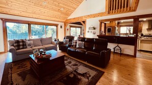 A spacious living area with a high ceiling, wooden beams, a sofa, a chair, and a coffee table. - Vista Chalet-Yosemite and Bass Lake getaway with Tesla charger (Oakhurst)