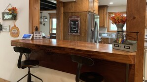 A bar area with wooden bar stools, a stainless steel refrigerator, and a chalkboard menu sign. - Vista Chalet-Yosemite and Bass Lake getaway with Tesla charger (Oakhurst)