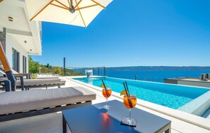 Area piscina con vista sul mare, due bicchieri su un tavolo e una sedia a sdraio.