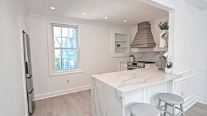 A modern kitchen with white cabinetry, a marble island, and two bar stools. - Harper House Downtown Mystic Romantic Weekend Getaway (Mystic)