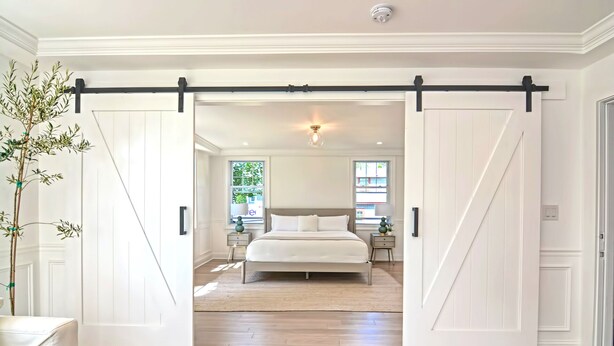A spacious bedroom with a large bed, two bedside tables, and a sliding barn door entrance. - Harper House Downtown Mystic Romantic Weekend Getaway (Mystic)