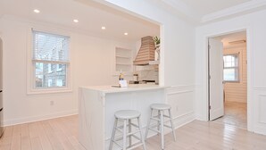 A modern kitchen with a white island, two bar stools, and a built-in oven. - Harper House Downtown Mystic Romantic Weekend Getaway (Mystic)