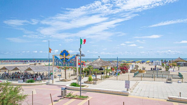 A beachside area with a large sign, a flag, and a beach umbrella. - Beach front apartment in Rosolina Mare with house sea view (Rosolina Mare)