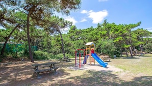 A playground with a slide and climbing structure, surrounded by trees. - Beach front apartment in Rosolina Mare with house sea view (Rosolina Mare)