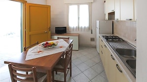 A compact kitchen with a dining table set for two, a small television, and a stove. - Beach front apartment in Rosolina Mare with house sea view (Rosolina Mare)