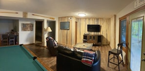 A living room with a pool table, a leather sofa, a television, and a wooden wall paneling.