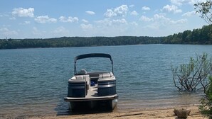 Ein Boot liegt an einer sandigen Küste, im Hintergrund ein See und bewaldete Hügel.