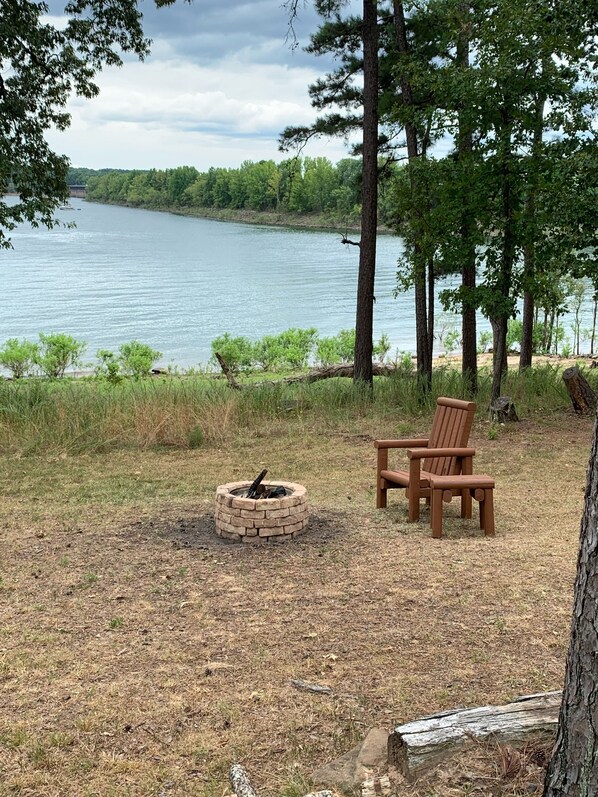 Un camping junto al lago, con una hoguera y sillas de madera.