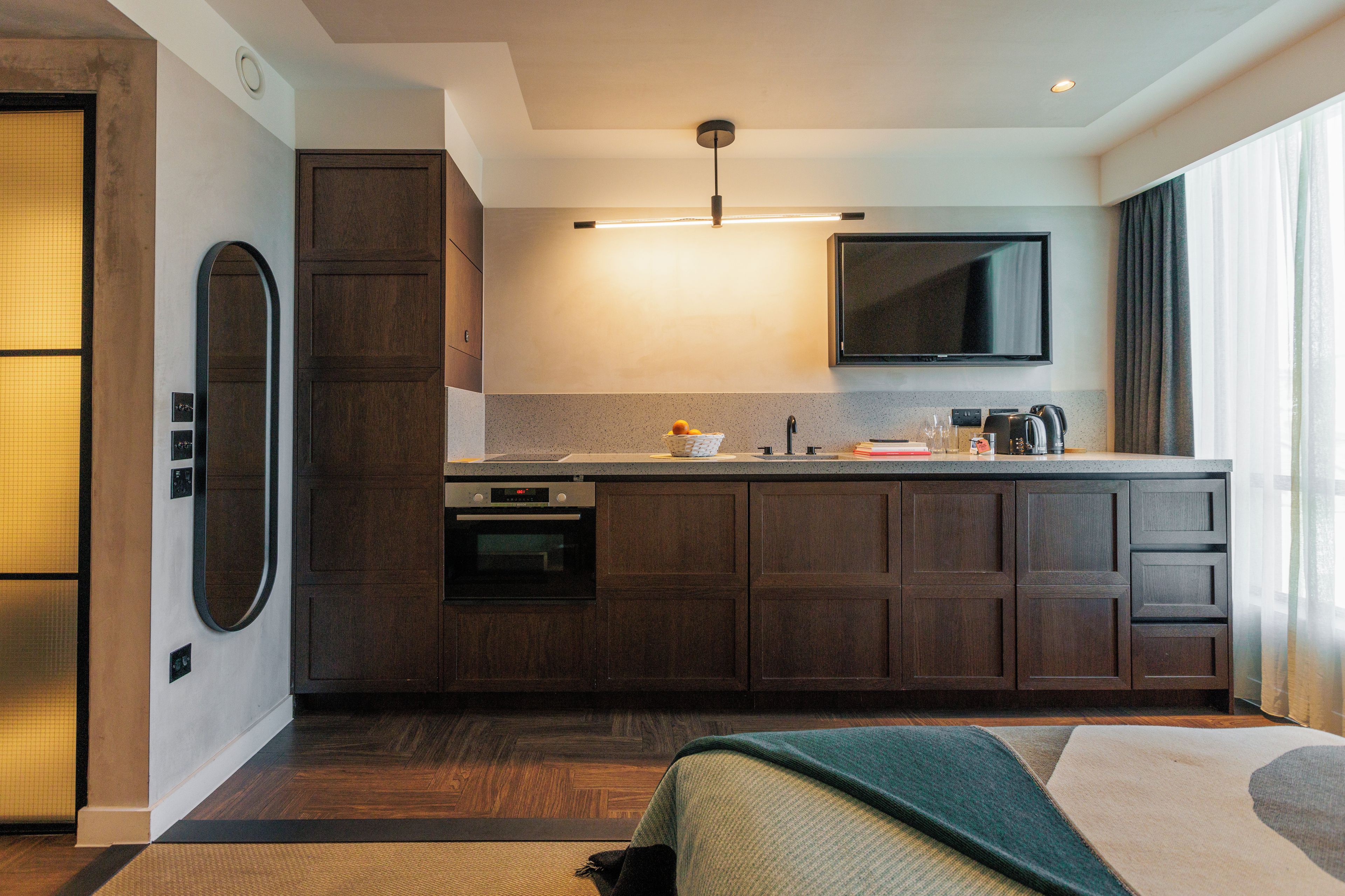 Habitació d'hotel moderna amb cuineta, televisió de pantalla plana i una finestra gran amb cortines.