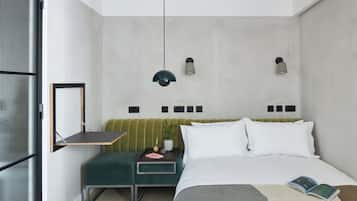 Un dormitorio moderno con un banco tapizado en verde, una mesita de noche con lámpara y una cama con edredón blanco.