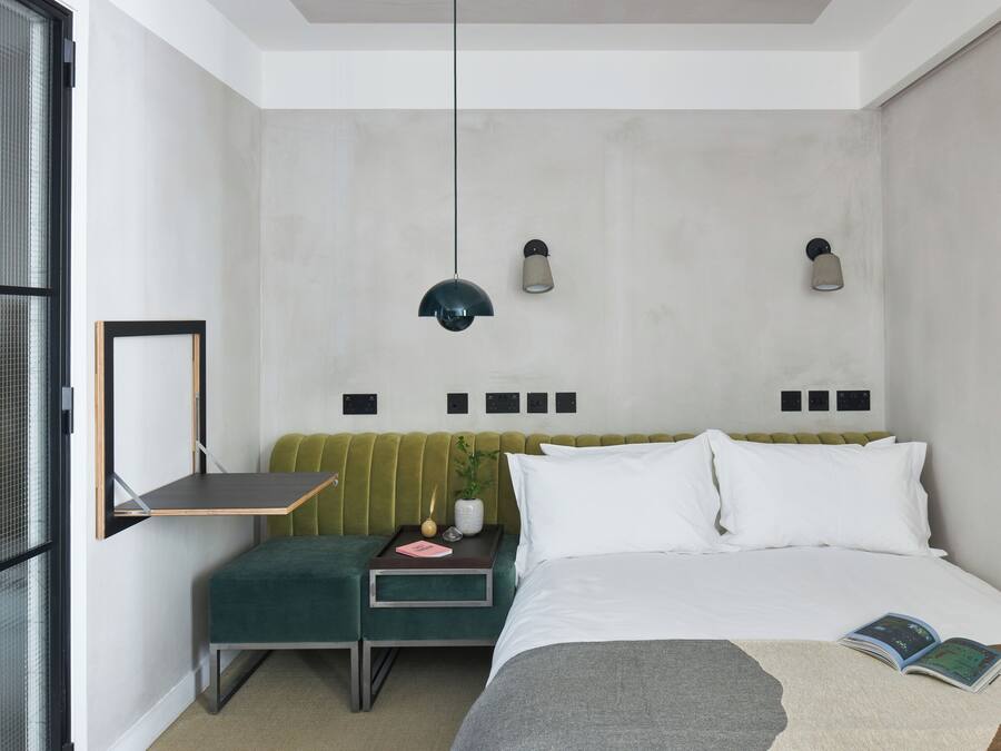 Un dormitorio moderno con un banco tapizado en verde, una mesita de noche con lámpara y una cama con edredón blanco.