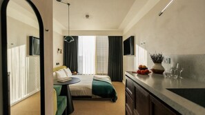 Quarto de hotel com cama, escrivaninha, área de refeições e bancada de cozinha.