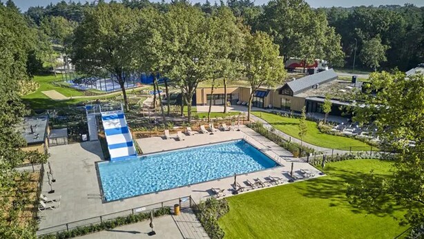 A large swimming pool with a blue and white slide, surrounded by trees and a grassy area.
