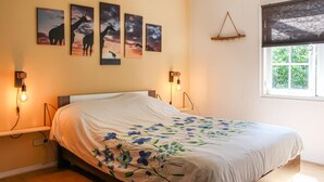 A bedroom with a bed, floral bedspread, wall art, and a window with a view.