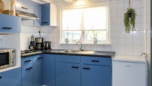 A kitchen with blue cabinets, a stainless steel sink, a microwave, a coffee maker, and a refrigerator.