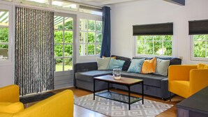 A modern living room with a grey sofa, yellow armchairs, and a coffee table. Large windows offer views of greenery outside.