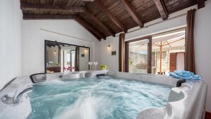 A hot tub with a stone exterior, a wooden ceiling, and a view of an outdoor patio with a table and chairs. - Cozy home in Bale with sauna (Bale)
