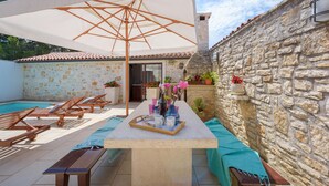 A patio with a pool, wooden lounge chairs, a table with a tray of items, and a stone wall. - Cozy home in Bale with sauna (Bale)