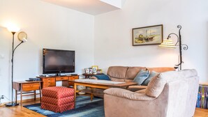 Ein Wohnzimmer mit Flachbildfernseher, einer Couch, einem Couchtisch und einem Schreibtisch mit Computer.