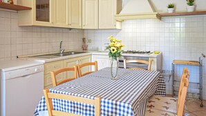 A kitchen with a checkered tablecloth, a vase with flowers, and a gas stove. - Agriturismo Le Cannelle (Pieve di Santa Luce)