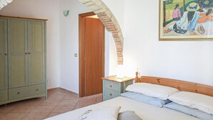 A bedroom with a bed, a nightstand, a green wardrobe, and a door leading to another room. - Agriturismo Le Cannelle (Pieve di Santa Luce)