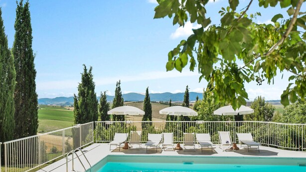 A pool area with lounge chairs and umbrellas, surrounded by a white fence and overlooking a scenic landscape. - Agriturismo Le Cannelle (Pieve di Santa Luce)
