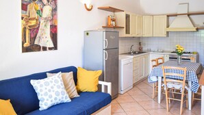 A compact living space with a blue sofa, a small kitchen with a refrigerator, and a dining area with a table and chairs. - Agriturismo Le Cannelle (Pieve di Santa Luce)