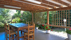 A covered patio with a wooden table and chairs, surrounded by a wooden fence and potted plants. - Agriturismo Le Cannelle (Pieve di Santa Luce)