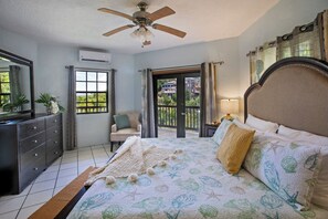 A bedroom with a bed, a dresser, a chair, and a balcony with a view. - Scenic Ocean View Villa: Mid-term and Long-Term stays (St Thomas)