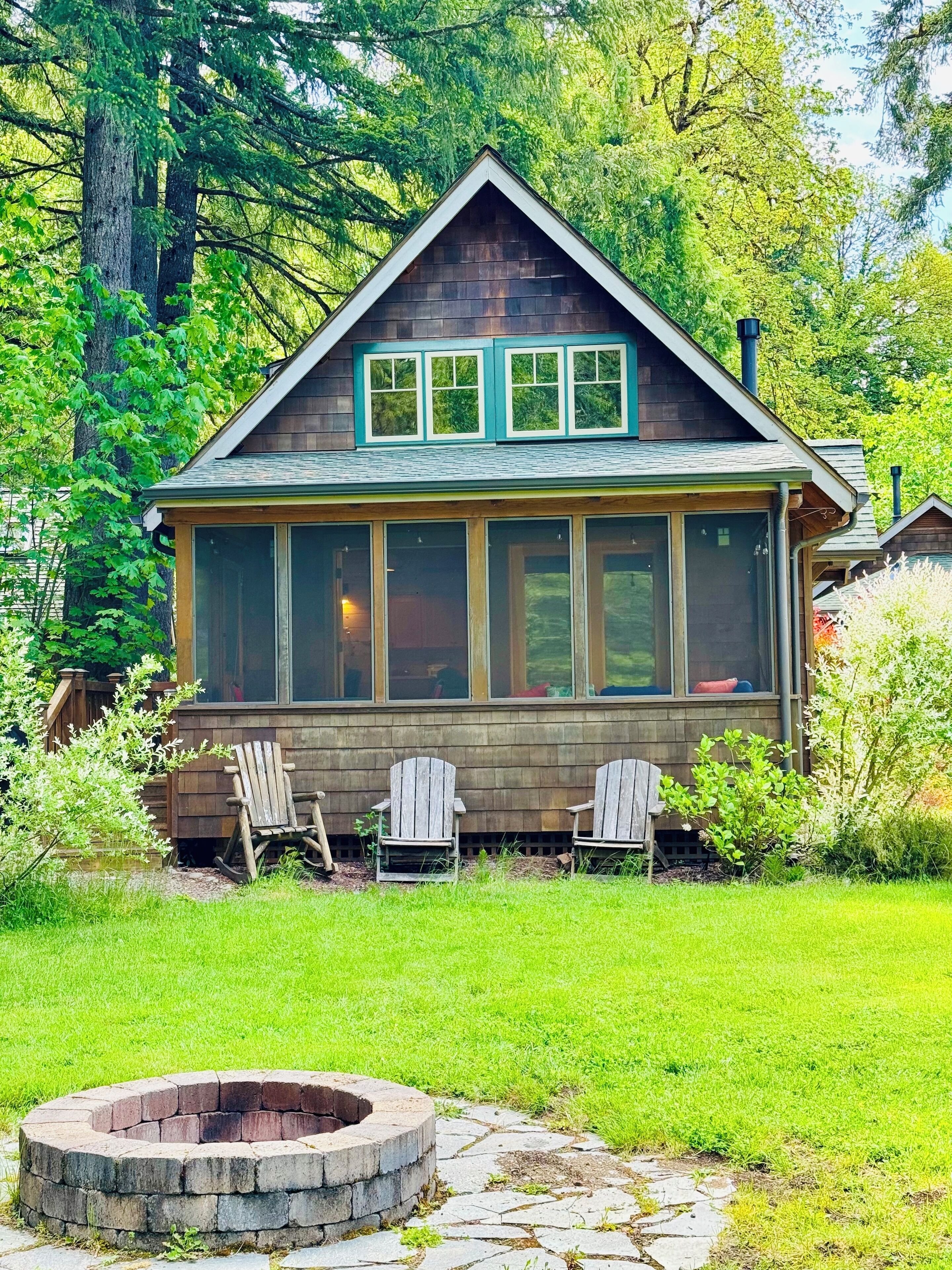 Een houten hut met een ruime veranda, twee Adirondack stoelen en een vuurkuil van steen.