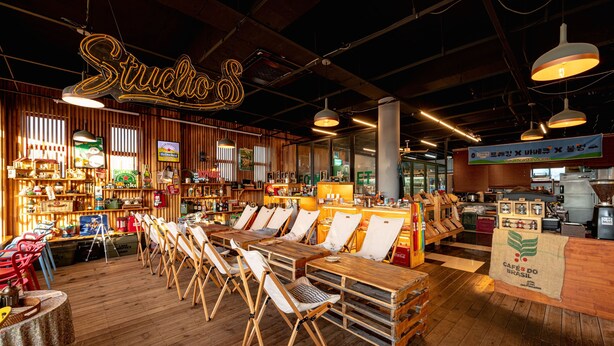 Een restaurantinterieur met houten tafels en stoelen, een neonbord en verschillende etenswaren.