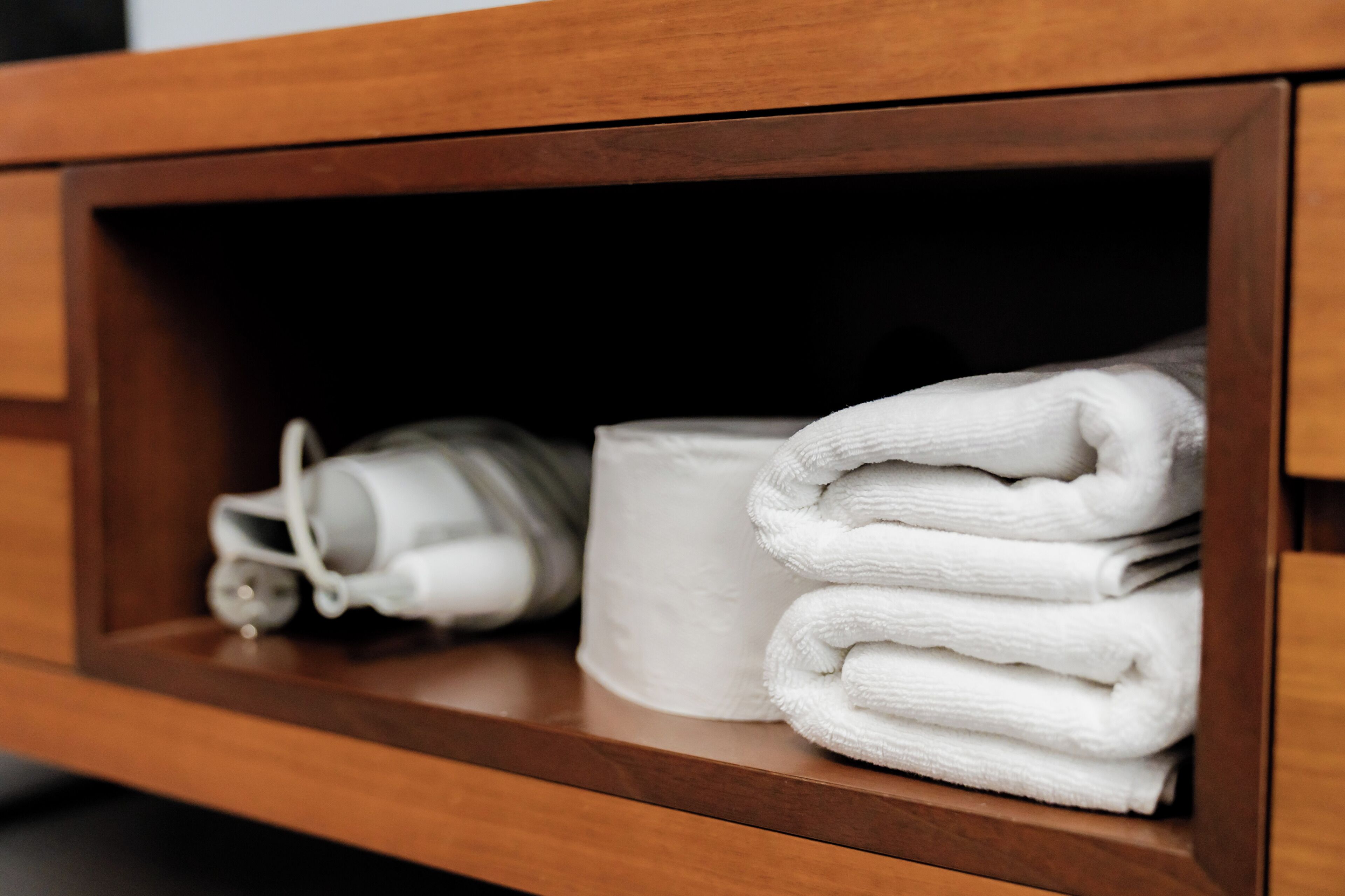 A wooden shelf with a rolled-up towel and a cylindrical object.