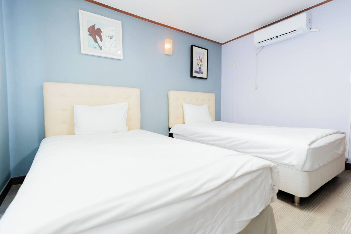A hotel room with two beds, a wall-mounted air conditioner, and framed artwork.