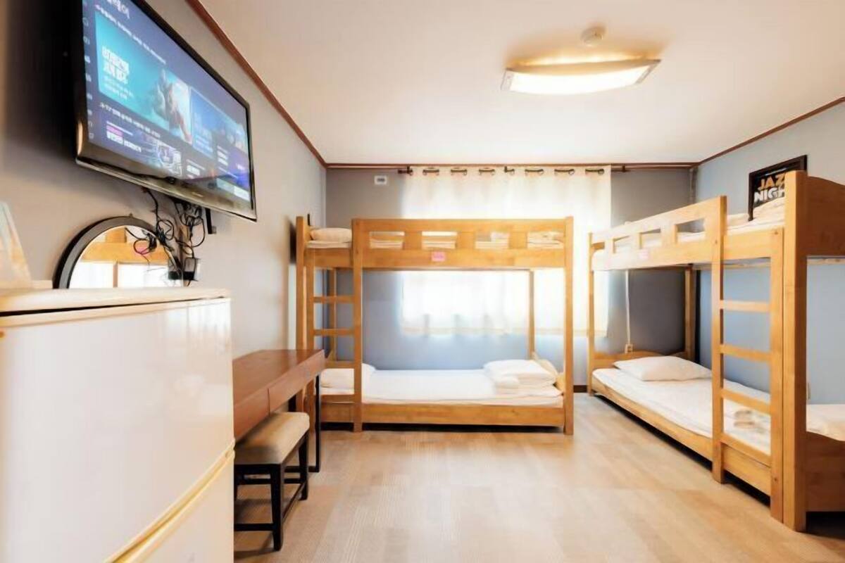 A room with bunk beds, a TV mounted on the wall, and a desk with a chair.