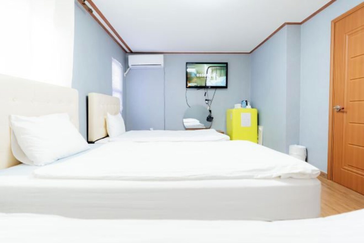 A bedroom with a bed, a television mounted on the wall, a yellow cabinet, and a door.