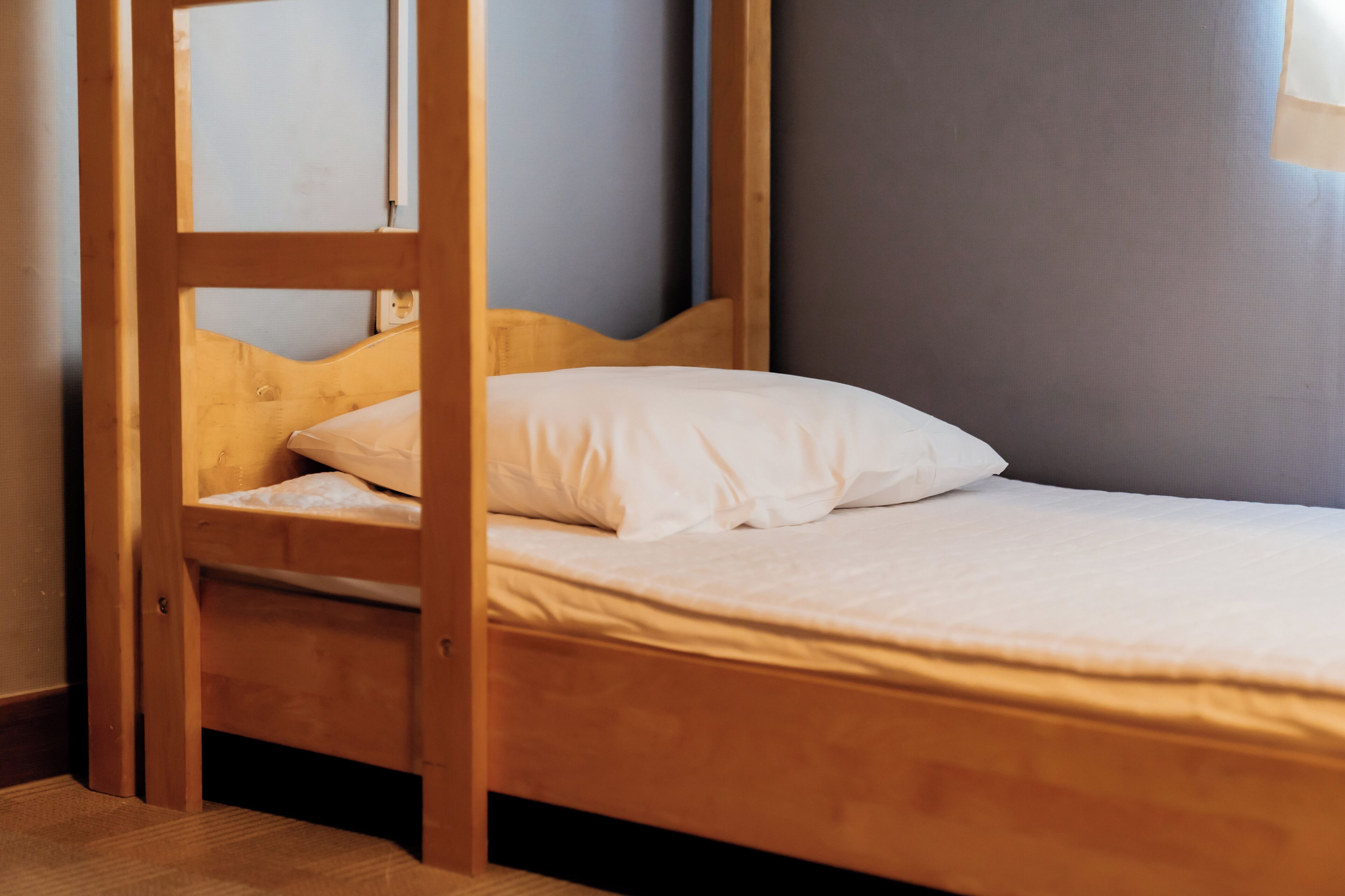 Una cama litera con estructura de madera, colchón blanco y almohada.