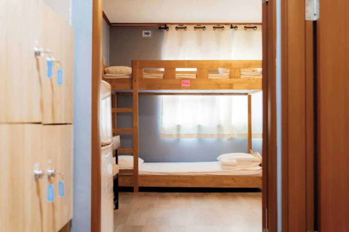 A bunk bed room with a wooden bunk bed, a ladder, and a window with curtains.