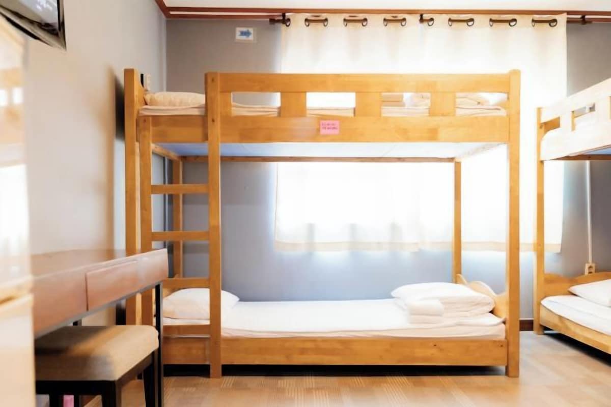 A bunk bed room with a wooden ladder, a bench, and a window with curtains.