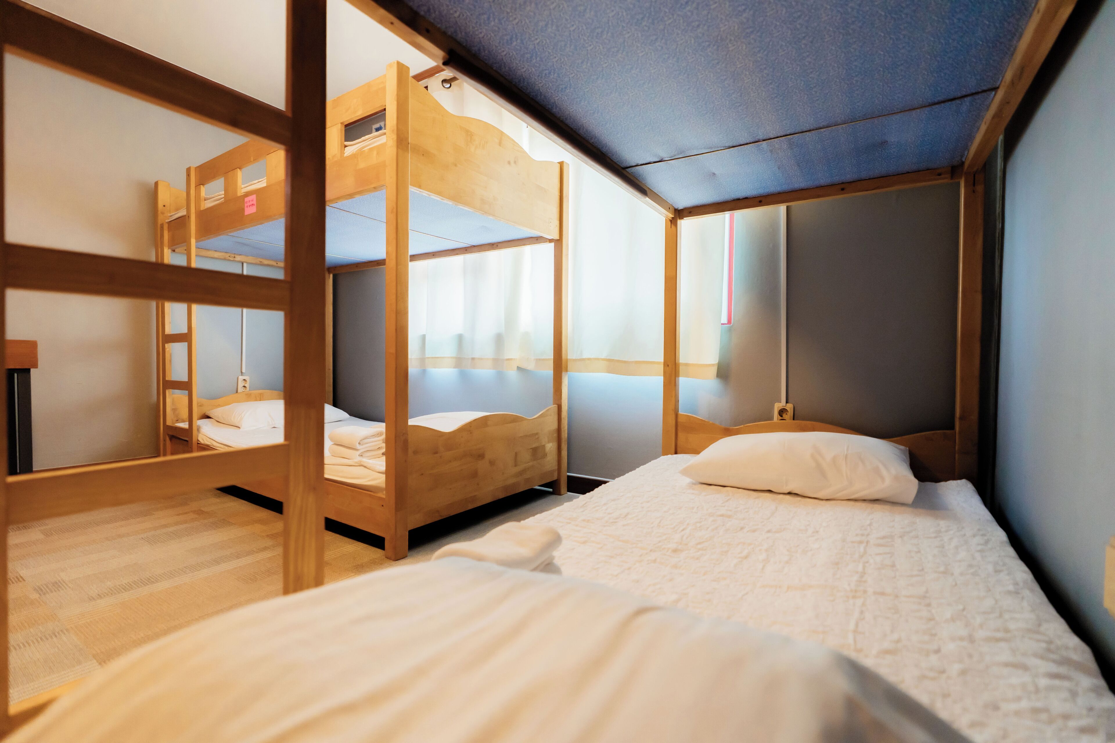 Una habitación con literas, piso de madera y ventana con cortinas.