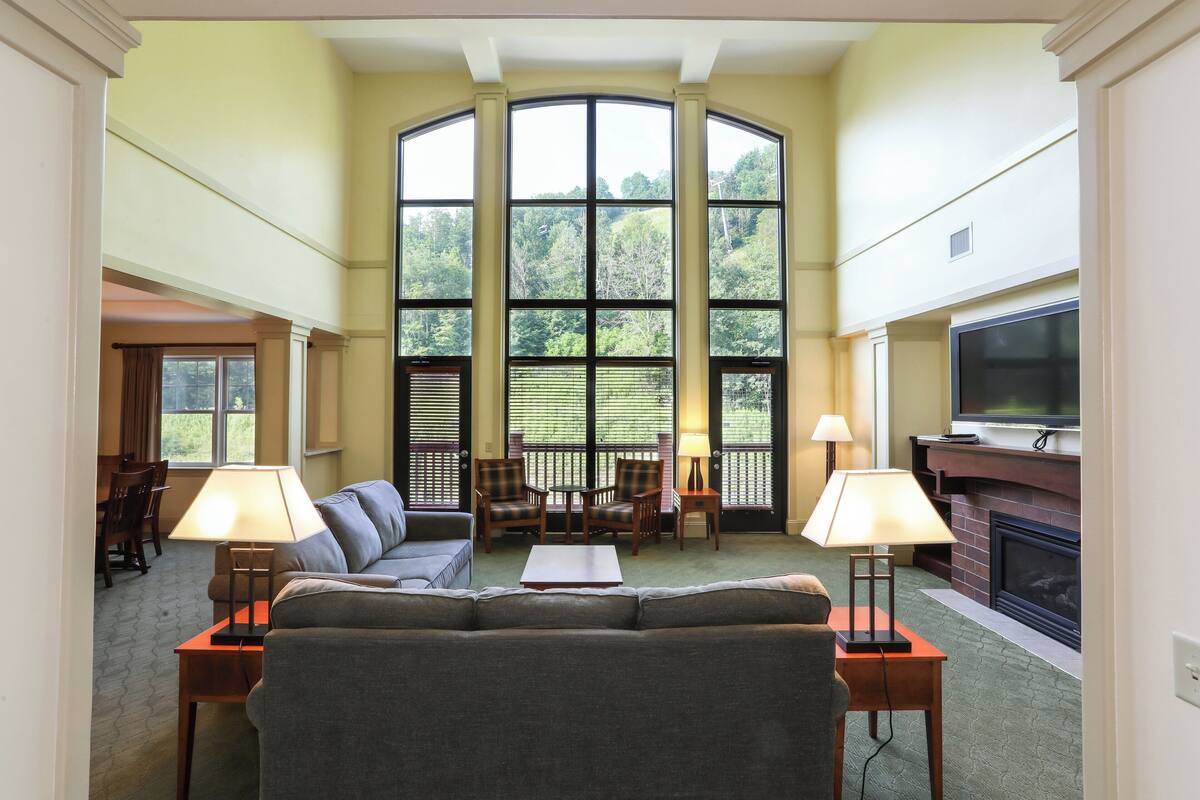 A spacious living room with a large window, a fireplace, and a television.