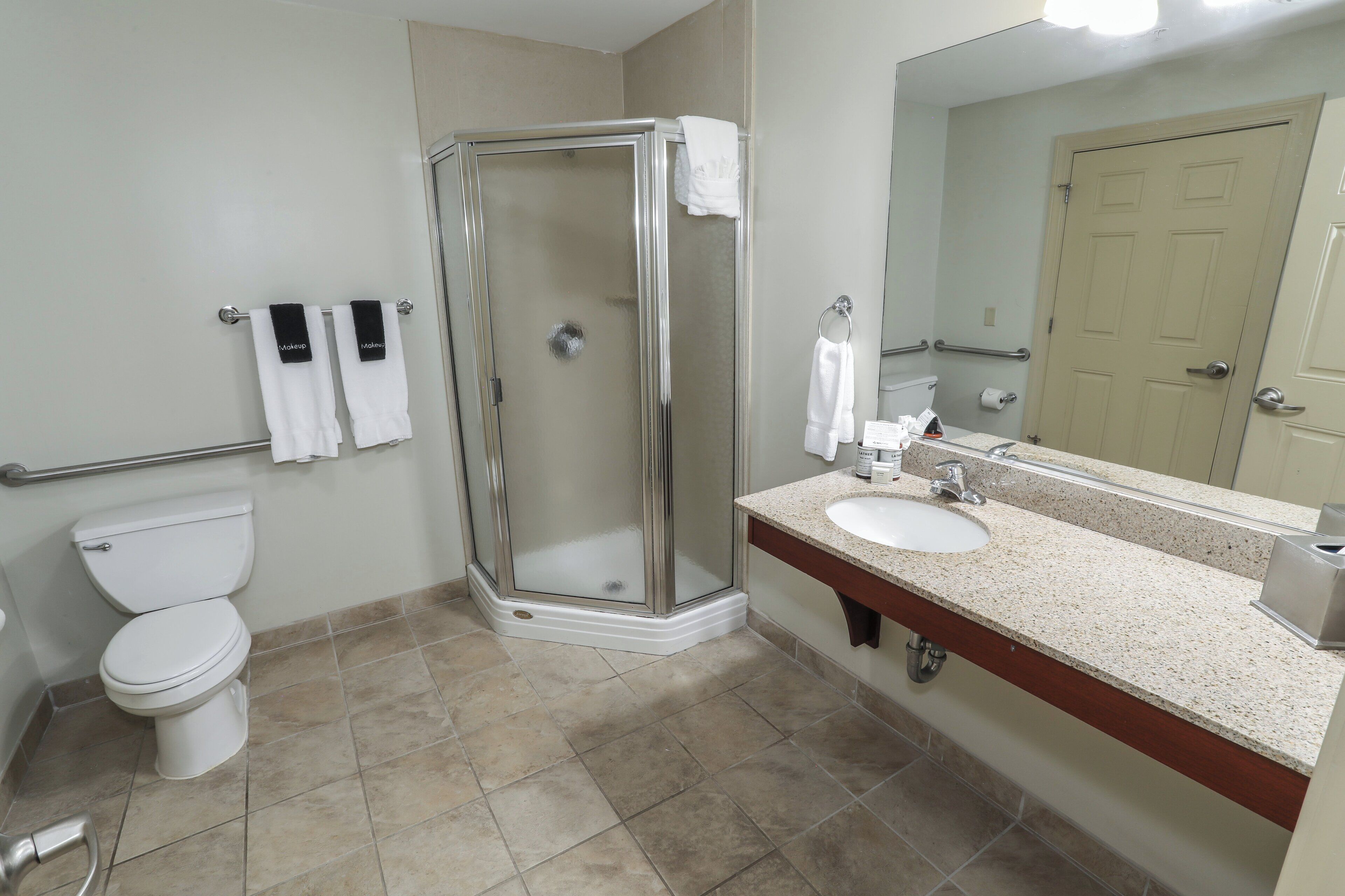 A bathroom with a glass-enclosed shower, a white toilet, a sink with a mirror, and two towels hanging on the wall.