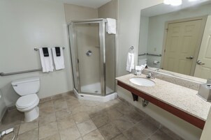 Un baño con ducha envuelta en vidrio, un inodoro blanco, un lavabo con espejo y dos toallas colgadas en la pared.
