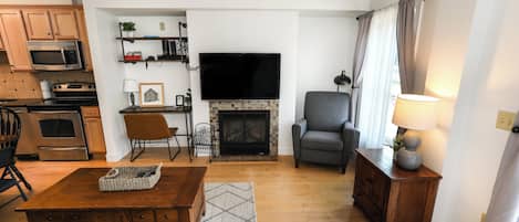 Una sala de estar con chimenea, televisor y comedor con armarios de madera y un microondas.