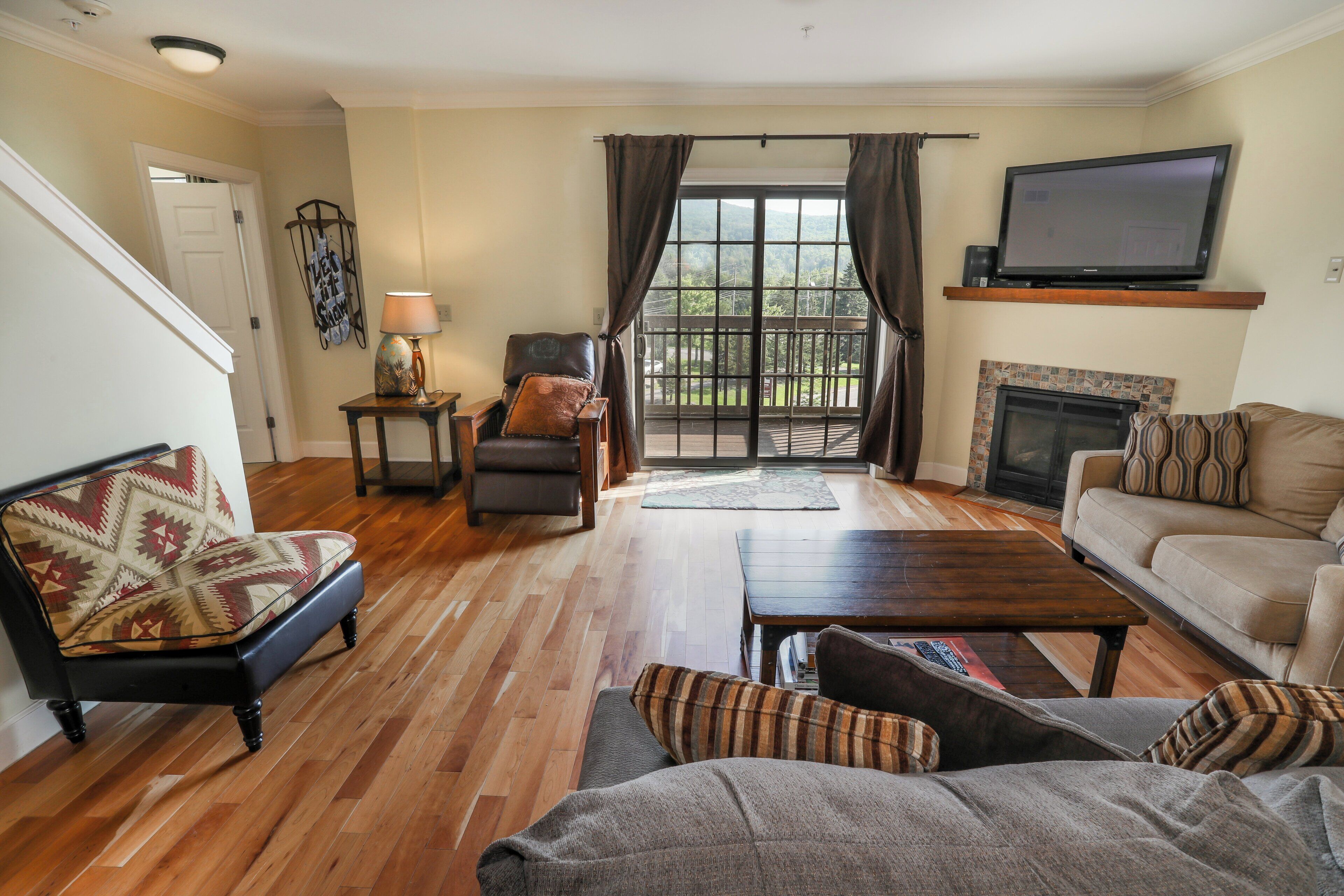 Una sala de estar con sofá, sillón y mesa de centro. Hay una chimenea y un televisor sobre un mueble.