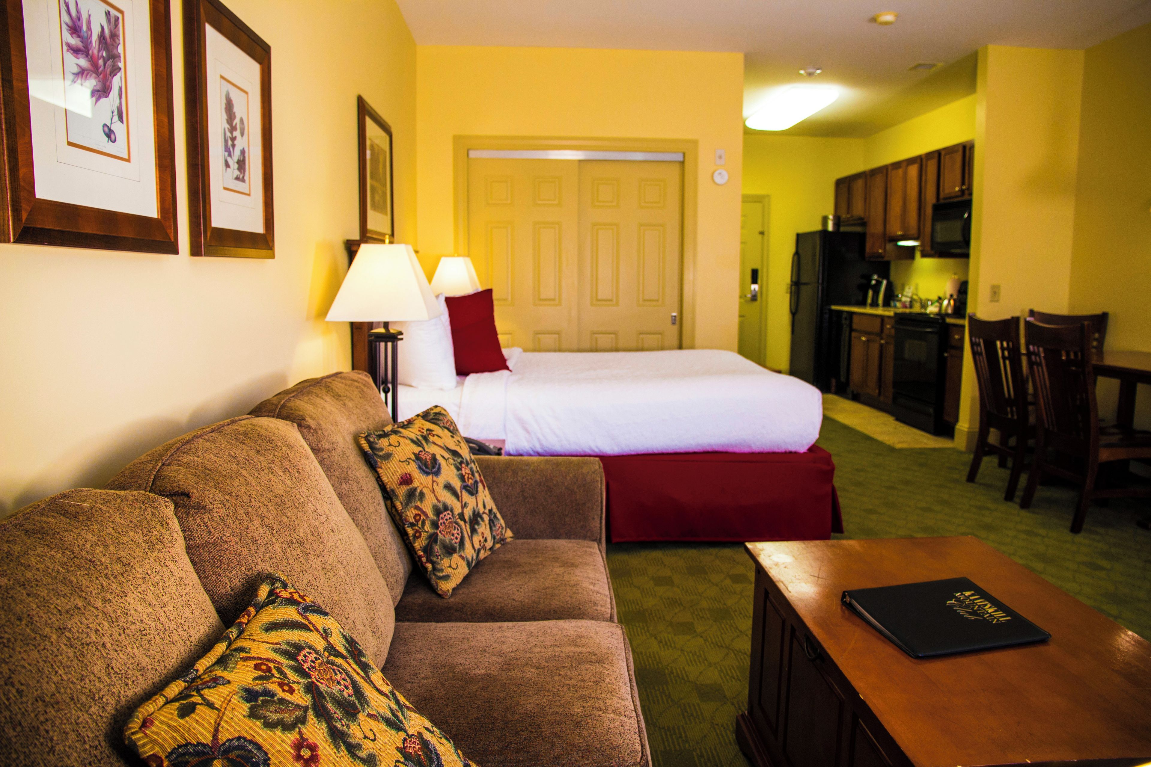 A hotel room with a bed, a sofa, a dining table, and a kitchen area.
