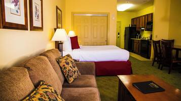 A hotel room with a bed, a sofa, a dining table, and a kitchen area.