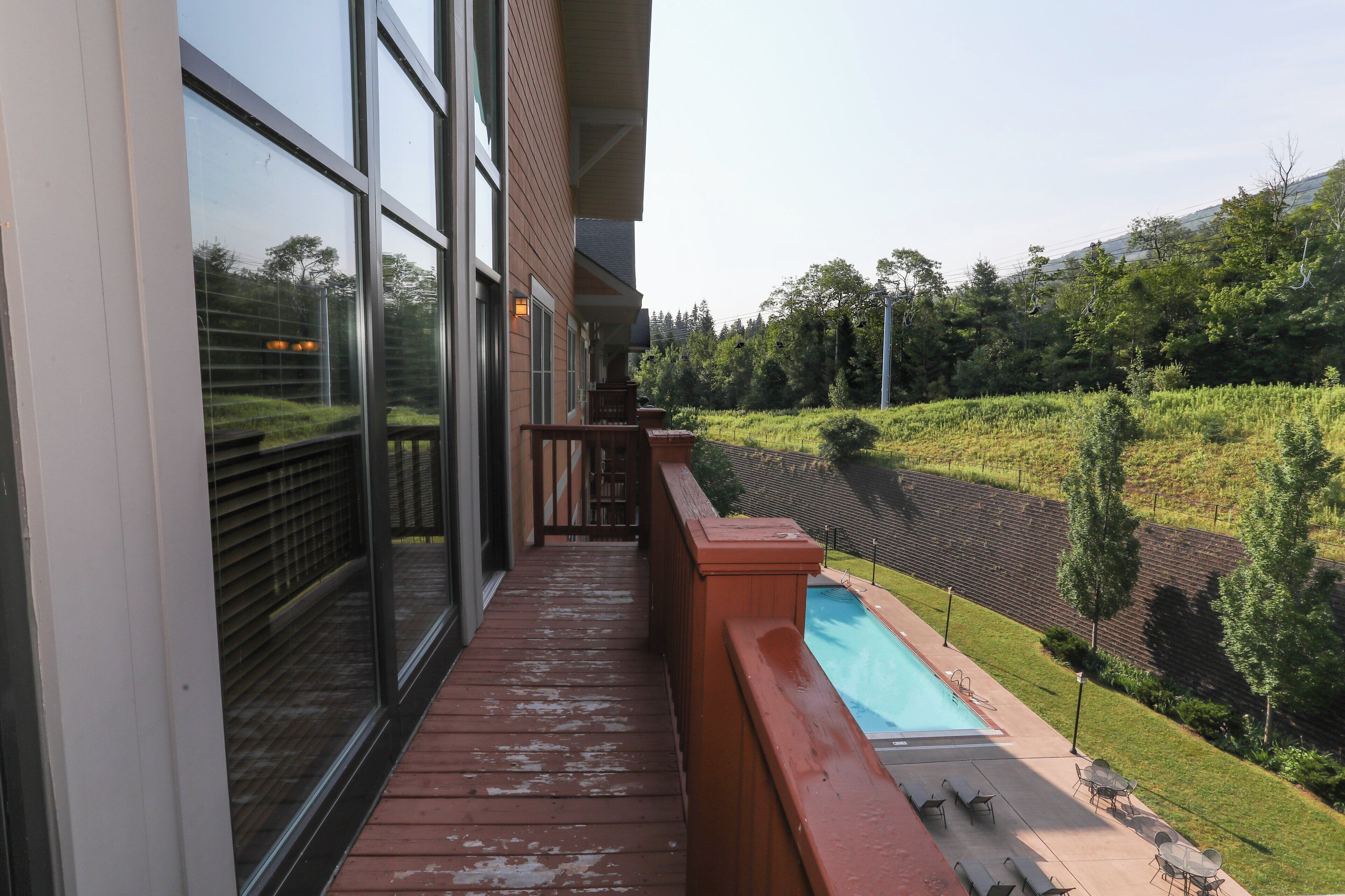 A balcony with a view of a swimming pool and a landscaped garden.