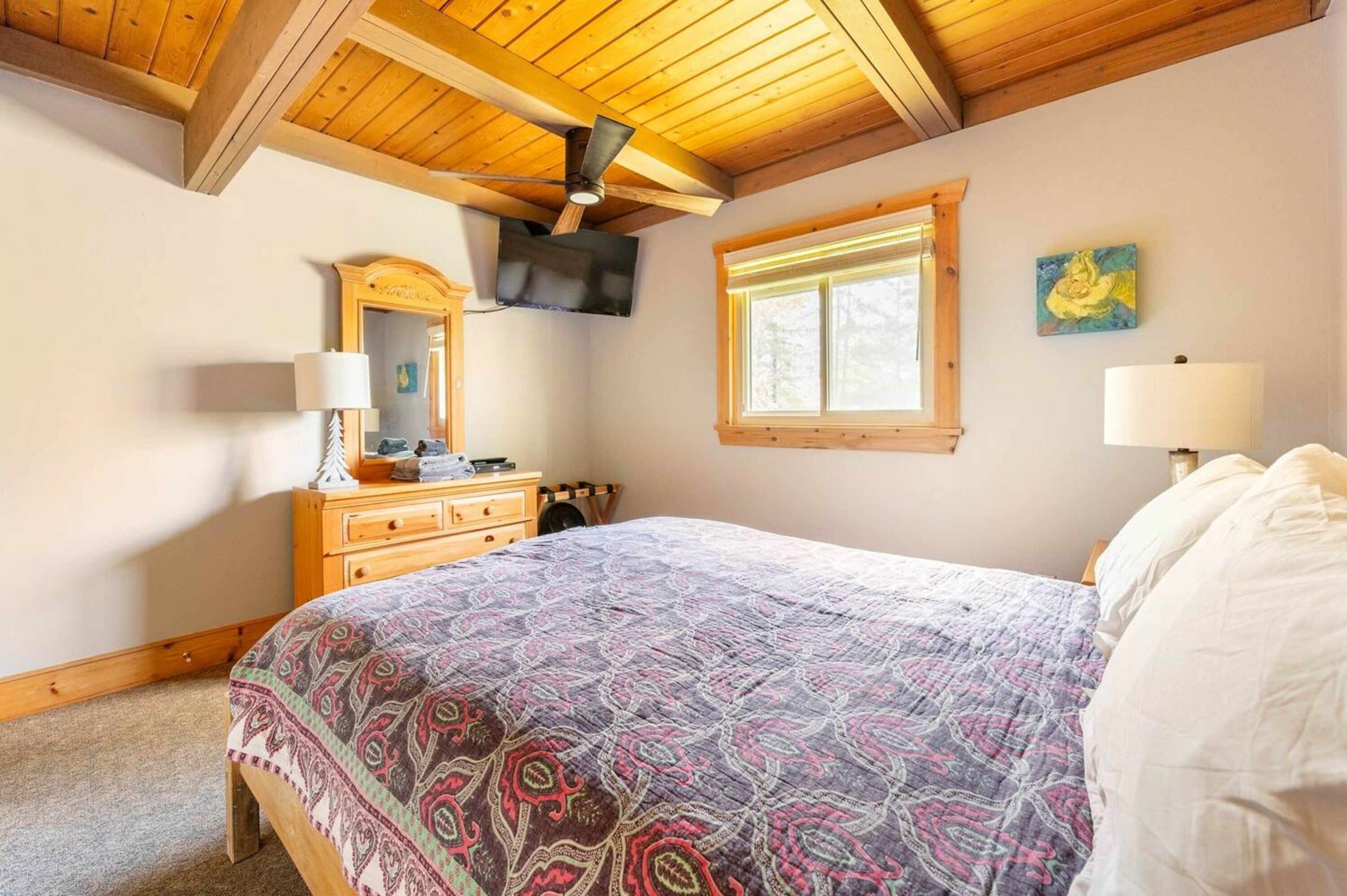 A bedroom with a bed, wooden headboard, ceiling fan, dresser, mirror, and a window with blinds.