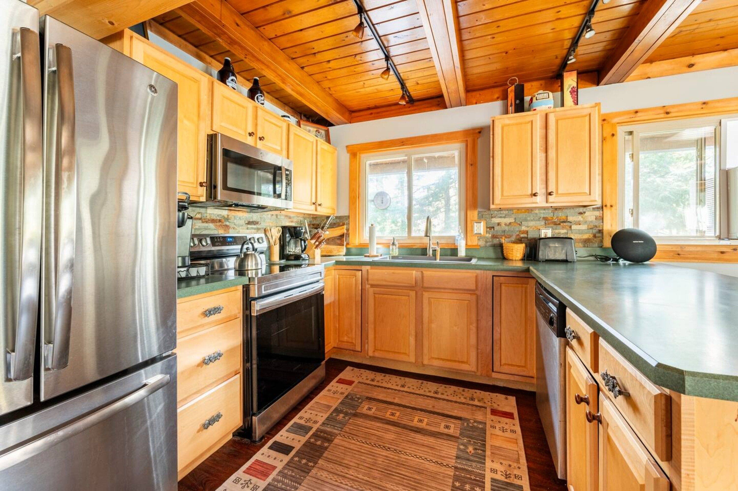 A modern kitchen with wooden cabinets, stainless steel appliances, and a large window.
