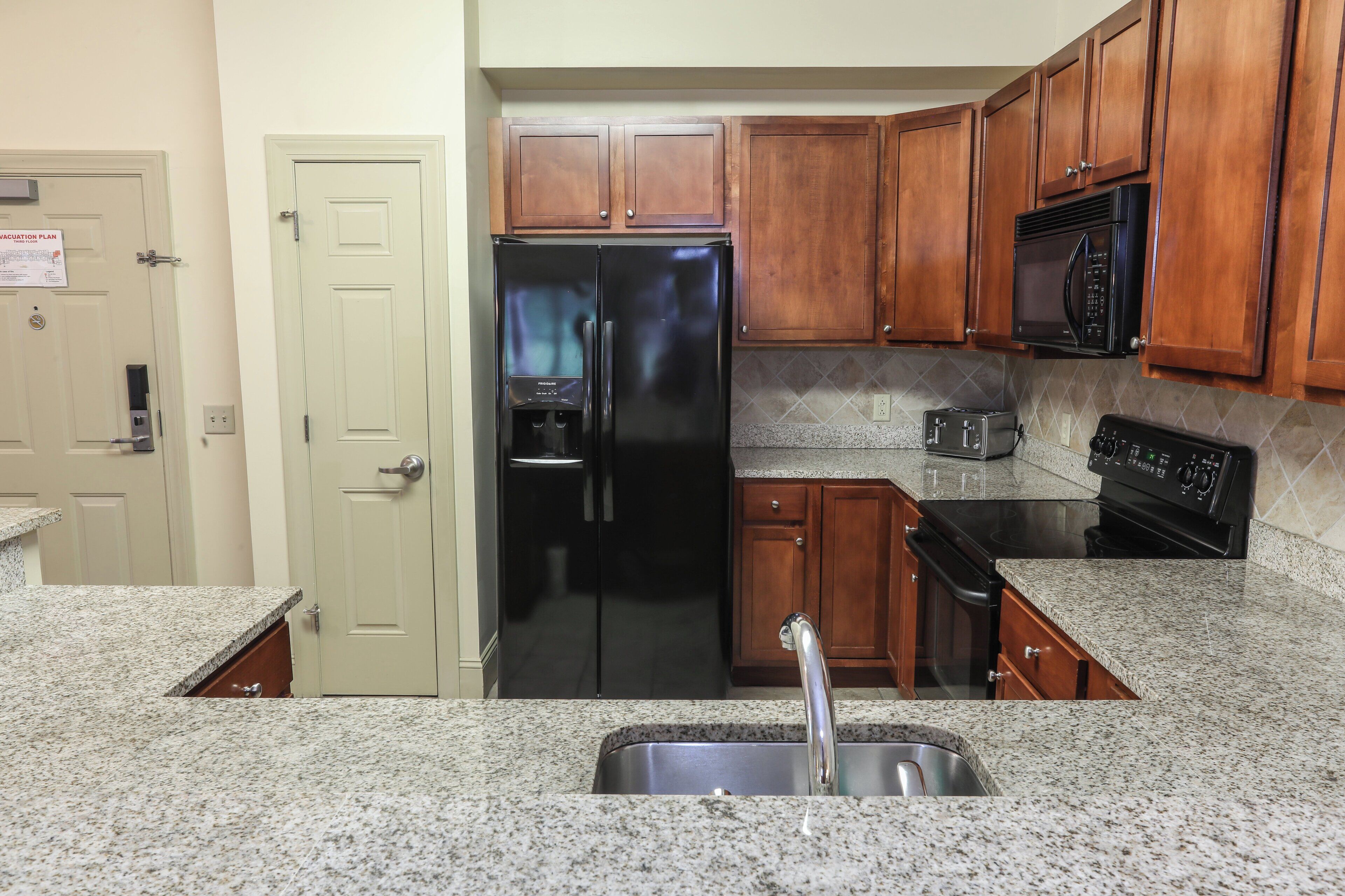 Una cocina con encimeras de granito, refrigerador de acero inoxidable, gabinetes de madera, microondas y estufa.